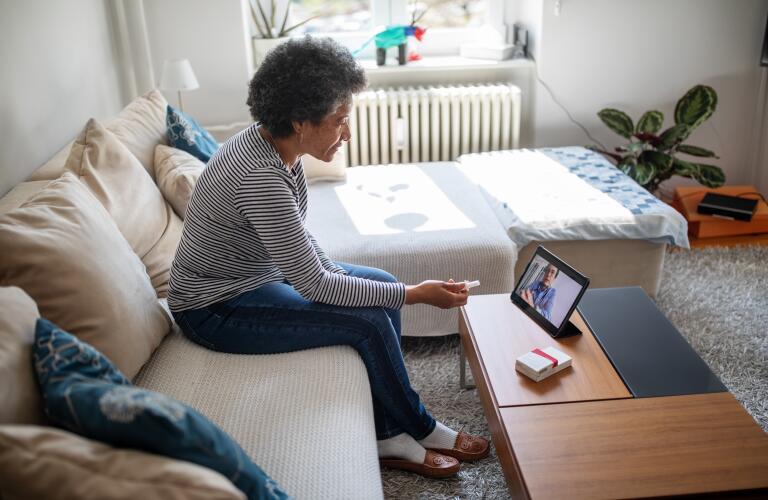 senior African American woman sitting on sofa in front of computer tablet during telehealth appointment