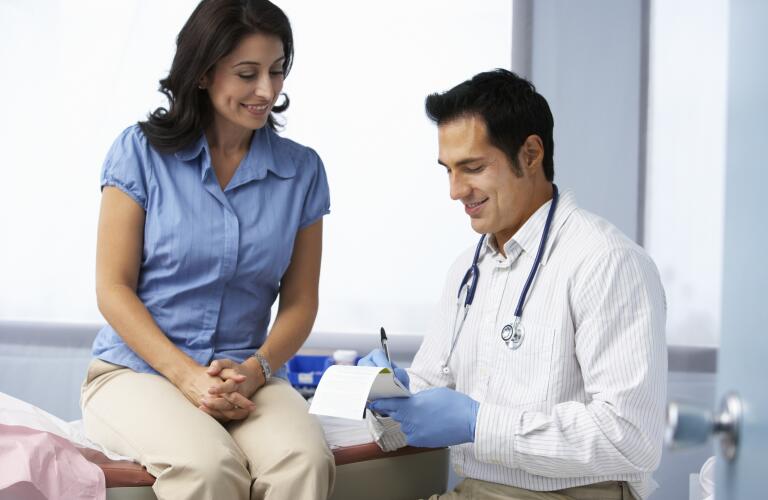 Doctor In Surgery With Female Patient Writing Prescription