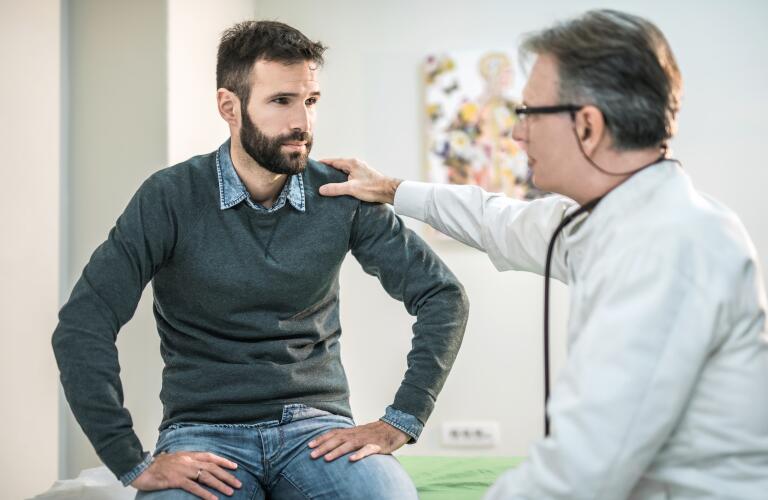 Middle age Caucasian male doctor talking to young male Caucasian patient with hand on shoulder