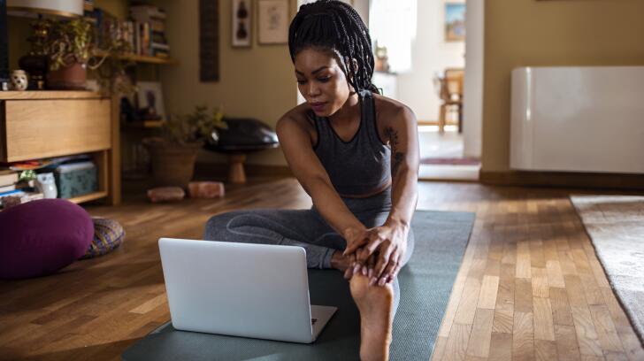 Woman learning yoga pose on floor with laptop