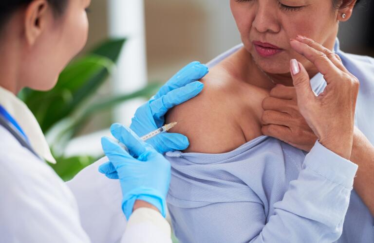 senior woman receiving vaccine injection in arm from nurse