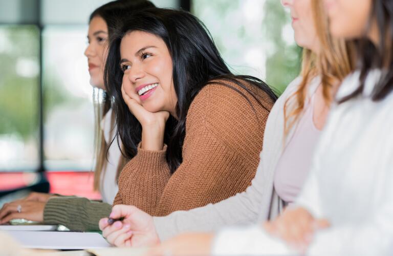 Young Hispanic woman in classroom smiling looking toward teacher