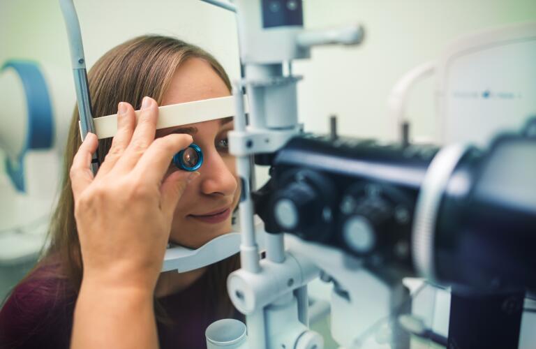 unidentifiable eye doctor holding lens up to female patient's eye to perform indirect ophthalmoscopy