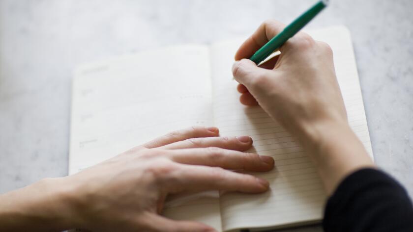 closeup of woman's hands making list in journal on table