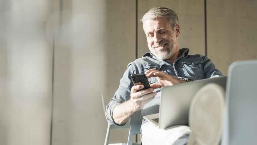 middle age man smiling at smartphone with laptop, working or socializing