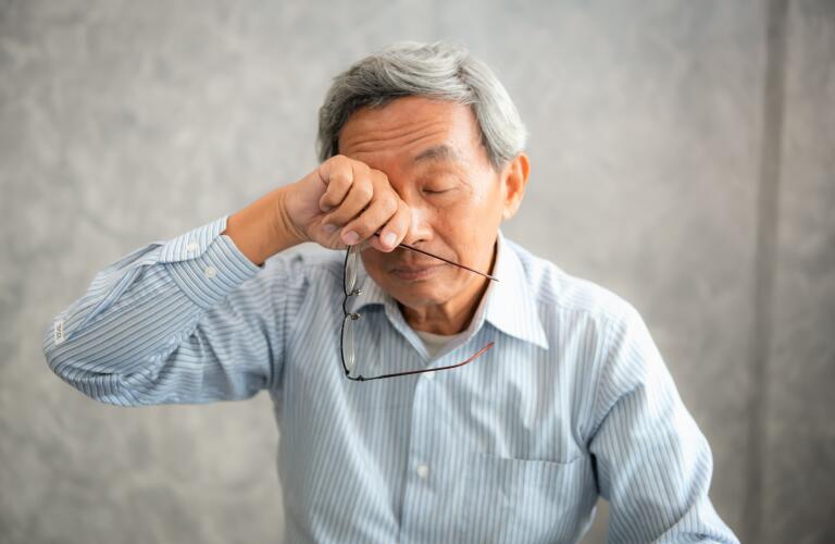 senior Asian male with eyeglasses rubbing eyes