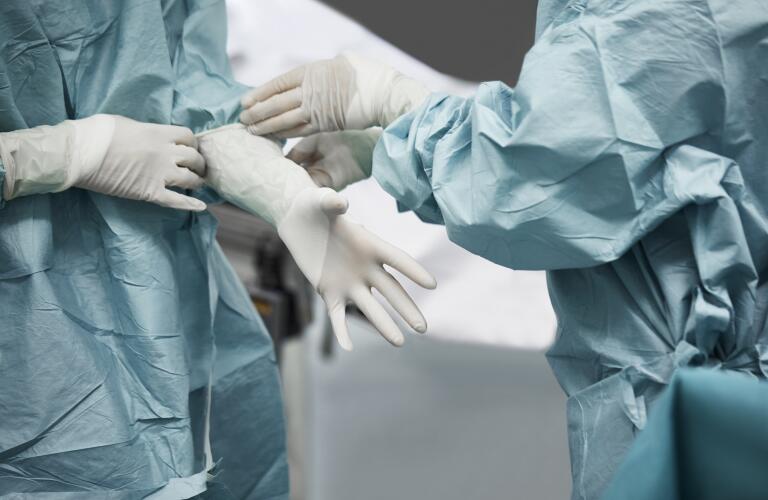 Cropped image of unseen doctors or surgeons in gowns putting on medical gloves