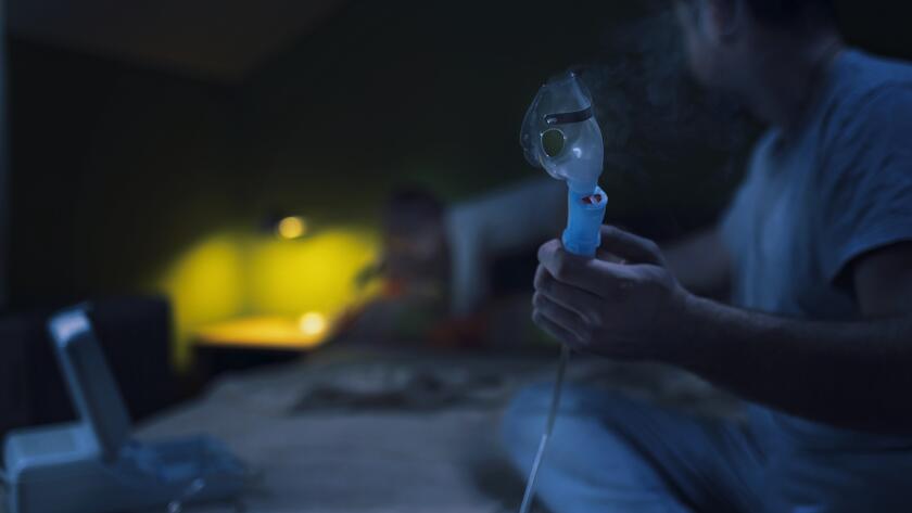 Man holding asthma nebulizer on bed at night