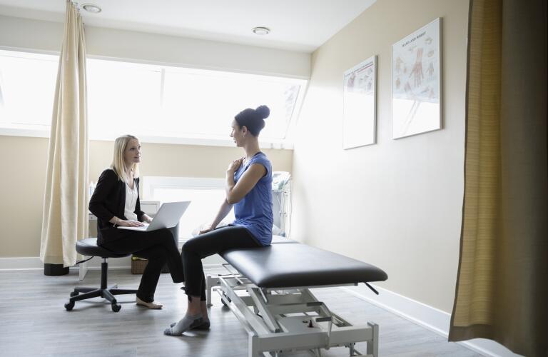 Young female Caucasian doctor talking to young female patient on exam table