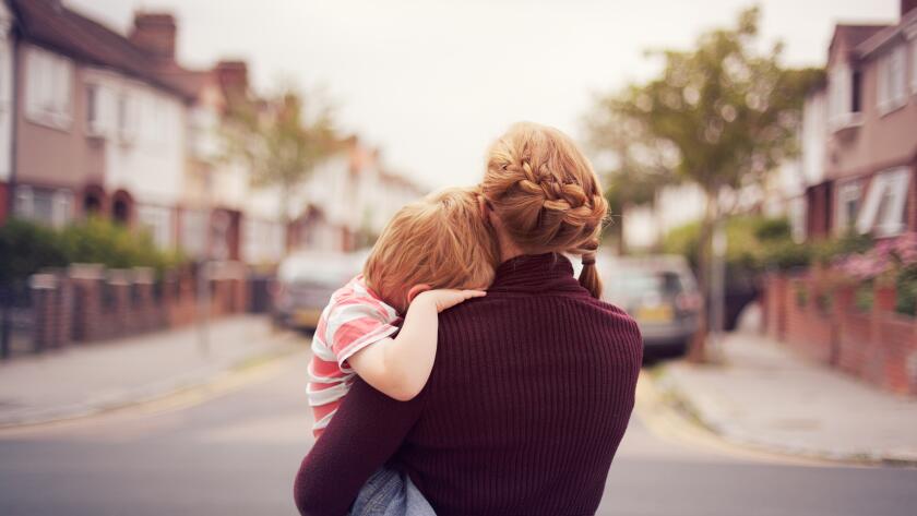 young boy held by his mother with head resting on her shoulder looking down a suburban street