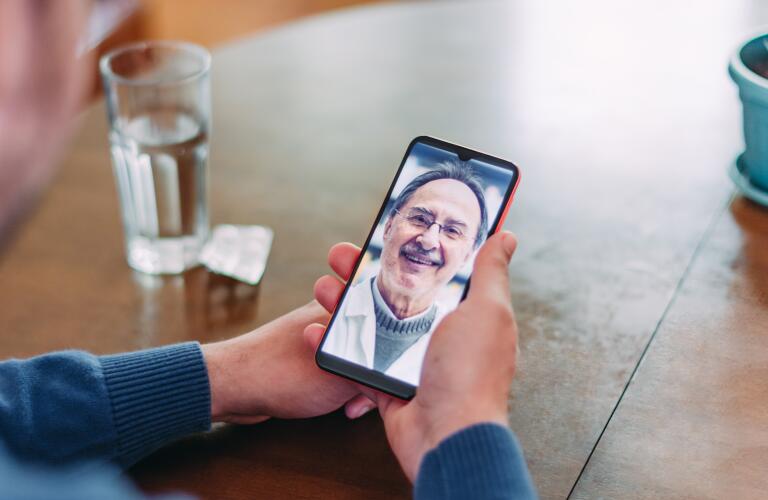 closeup of hands holding smartphone during telehealth appointment on dining table next to glass of water