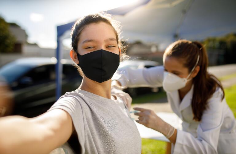 teen girl wearing face mask smiles as she take a selfie while getting vaccine outdoors at pop-up vaccine clinic