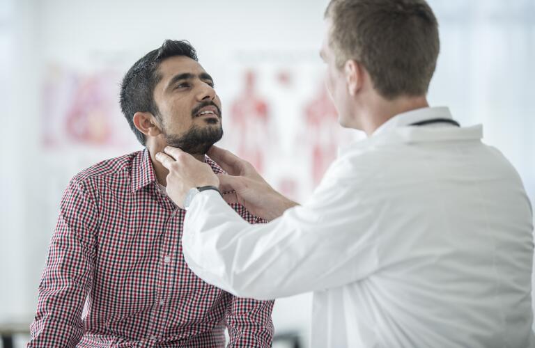 Hombre joven hispano o de Oriente Medio que se somete a un examen de tiroides o cuello por parte de un médico joven caucásico