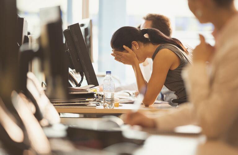 Young woman at work with head in hands from stress, fatigue or headache