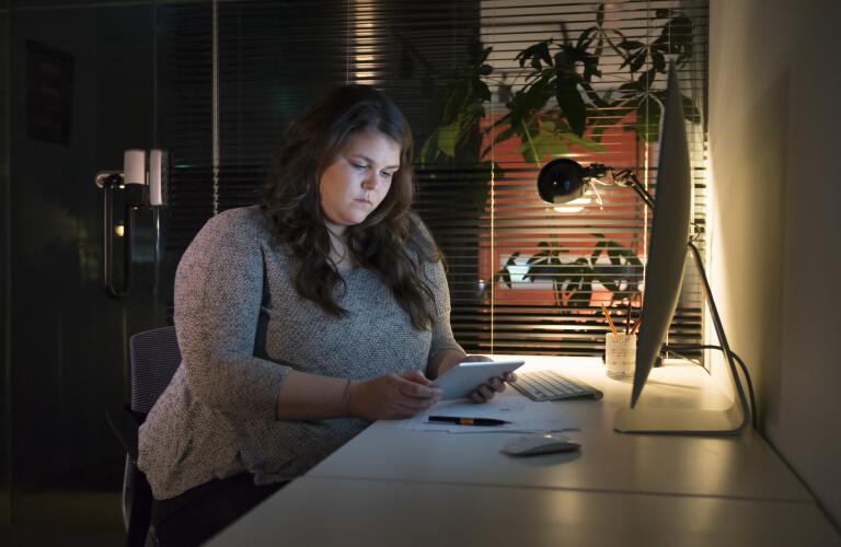 Young overweight Caucasian woman in office looking at tablet at desk