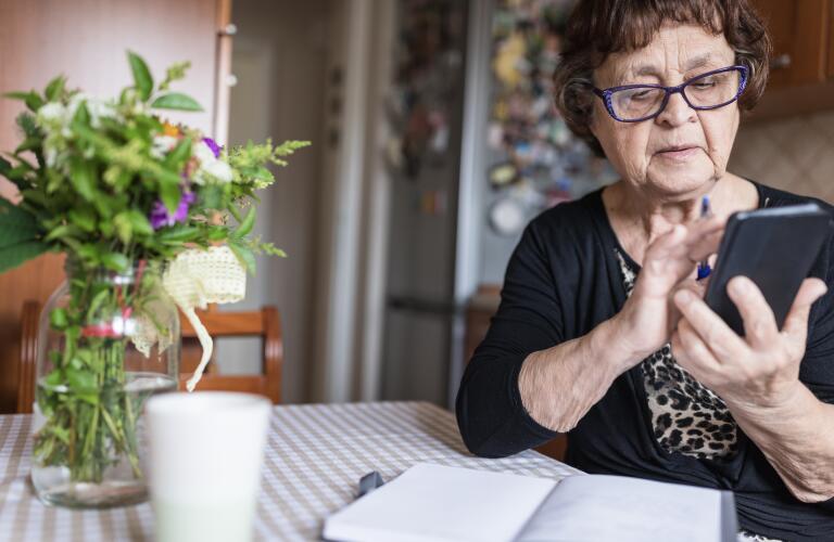 senior woman in her kitchen wearing eyeglasses when looking at smartphone