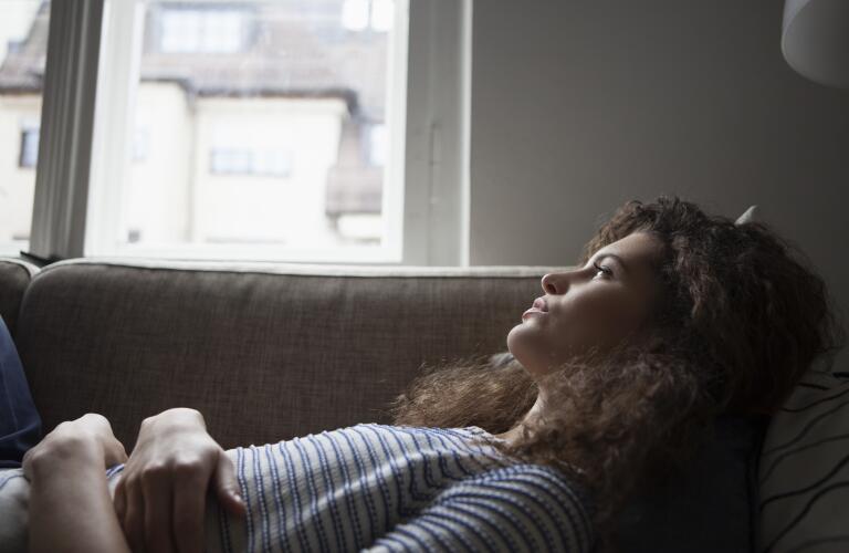 serious-woman-on-couch-with-stomach-pain