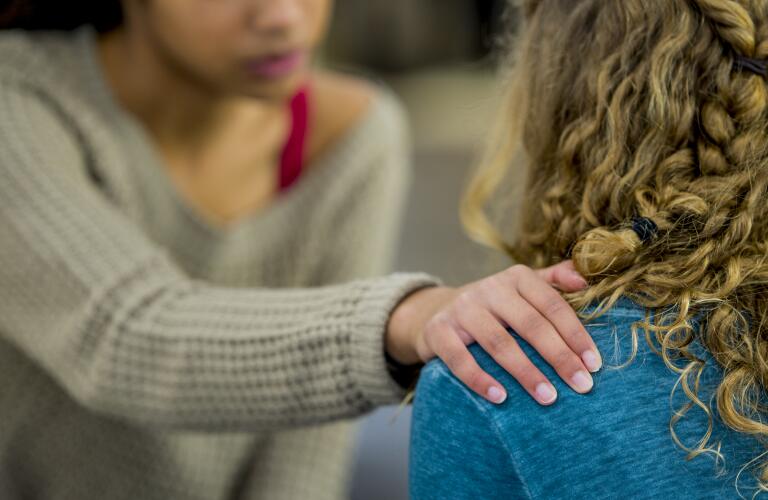 Unseen female woman comforts unseen female friend with hand on shoulder