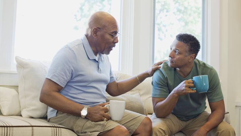 Senior father and son talking while having coffee on sofa