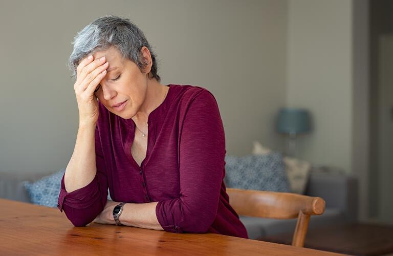 Senior Caucasian woman at table with head on hand from stress, fatigue or migraine headache
