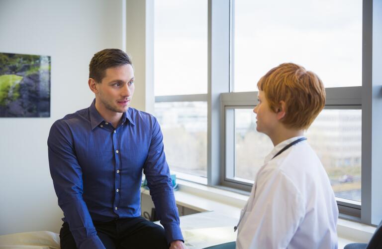 Young Caucasian male patient on exam table talking to young female Caucasian doctor