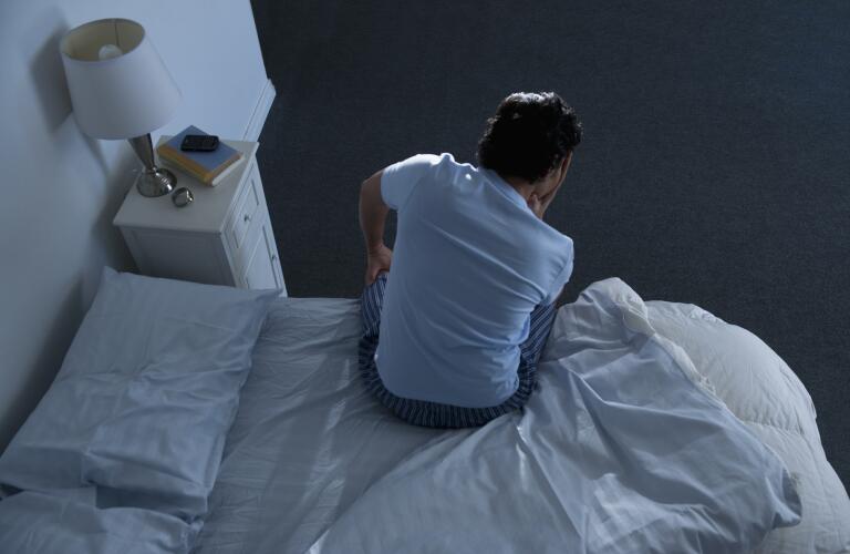man in low light sitting up in bed with head in hand