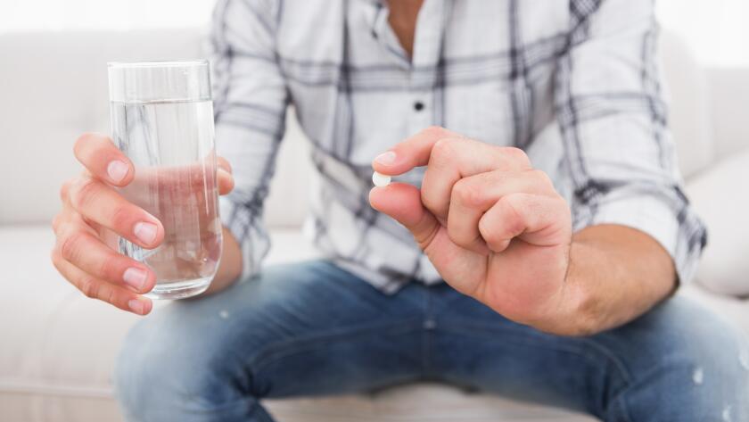 man-sitting-on-couch-holding-glass-of-water-and-pill