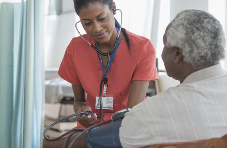 Caregiver taking blood pressure of older man in wheelchair