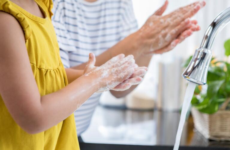 mother showing daughter how to wash hands with soap over sink