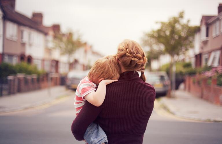 young boy held by his mother with head resting on her shoulder looking down a suburban street