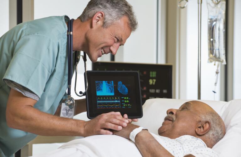 Middle age Caucasian male doctor smiling and talking to older African American male patient in hospital bed