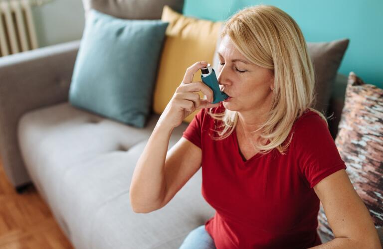 middle aged Caucasian woman sitting on couch using inhaler