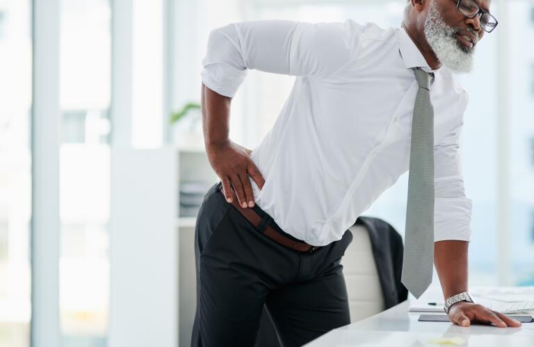Older African American businessman standing at desk with back pain