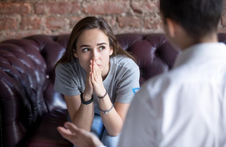 Young Caucasian girl in thought sitting on couch talking to therapist or counselor