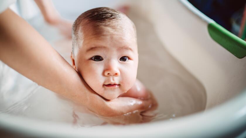 newborn baby held by mother's hands in small bathtub