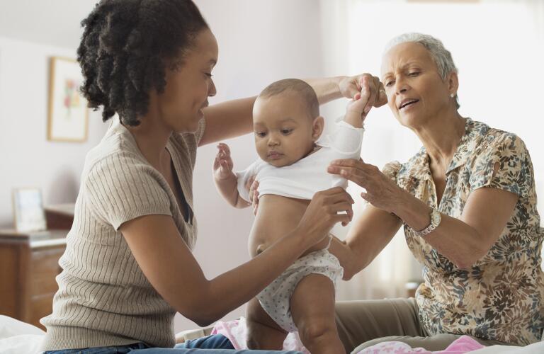 mother and granparent dressing infant in bedroom
