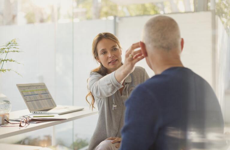 Female doctor helping male patient with hearing aid in doctors office