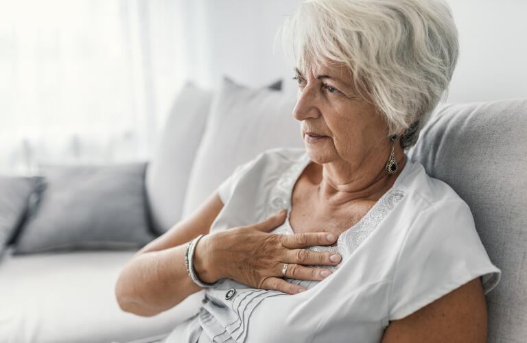 Mature Caucasian woman holding hand to chest sitting on couch