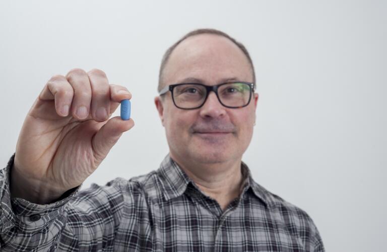 smiling middle aged Caucasian male holding PrEP HIV pill