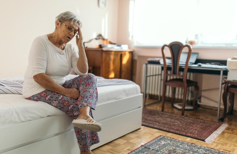 Senior Caucasian woman at edge of bed holding head with headache or fatigue