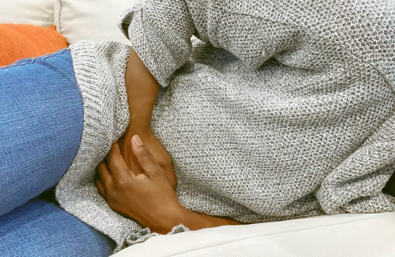 cropped shot of African American woman lying on sofa with pelvic pain