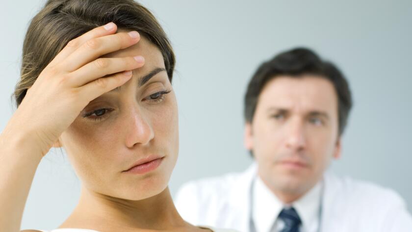 woman-with-hand-on-head-with-doctor-in-background
