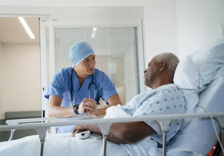 Older African American male patient in hospital bed talking to Asian American male surgeon