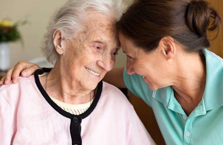 Elderly Caucasian woman smiling while being comforted by younger Caucasian caregiver