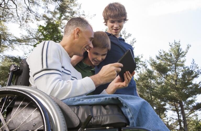 Man with spinal cord injury in wheelchair with his sons reading a tablet