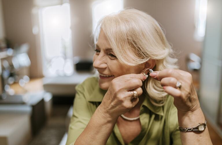 Senior Caucasian woman smiling as she puts in hearing aid