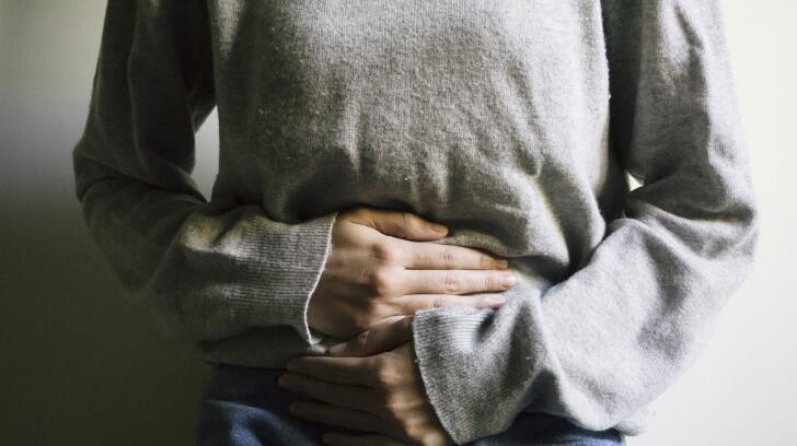 Cropped photo of young female Caucasian woman holding stomach in pain