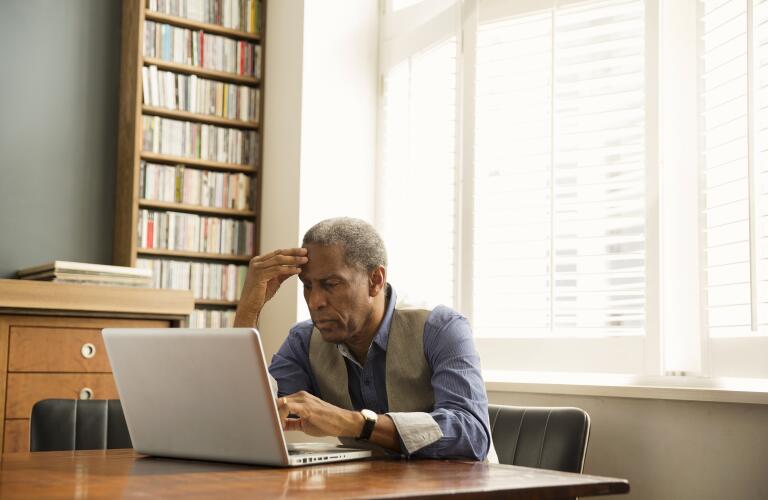senior African American man sitting in office study looking at laptop