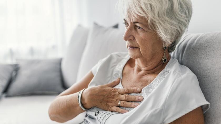 Mature Caucasian woman holding hand to chest sitting on couch