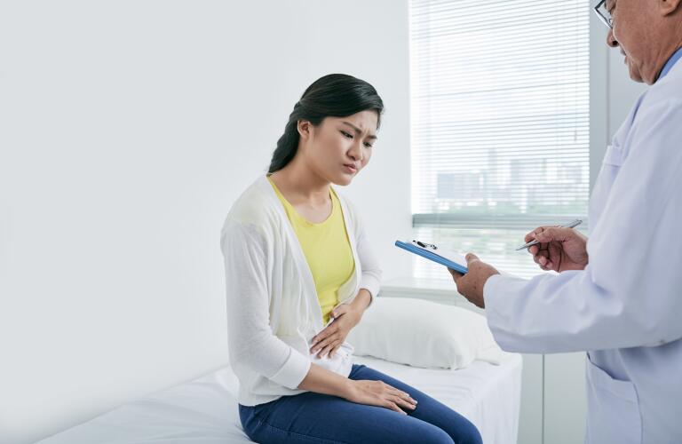 Young Asian woman suffering from stomach pain talking to doctor